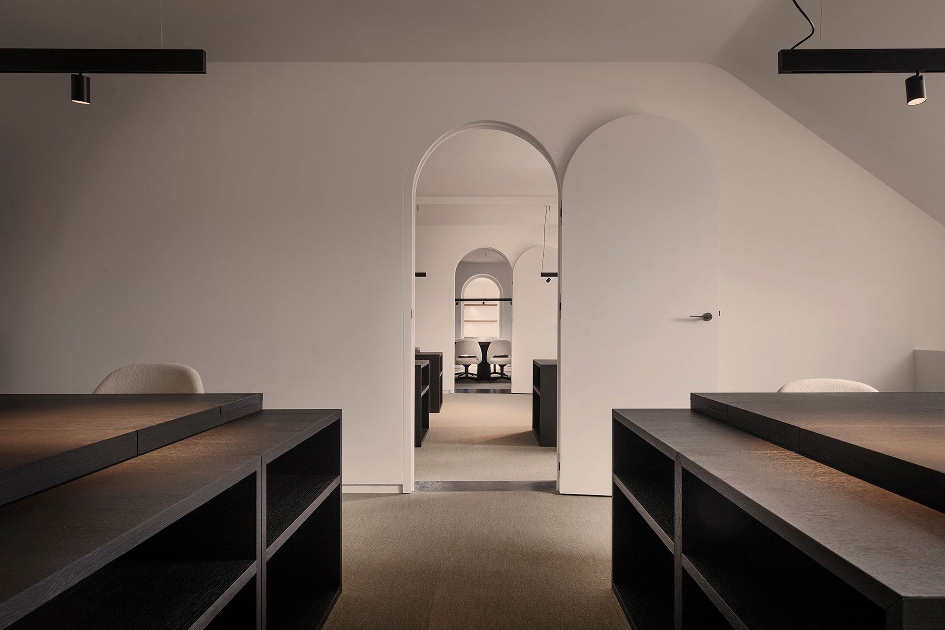 Custom interior office space featuring white walls, black wooden desks, green-toned carpet, and a suspended lighting system above the desks.