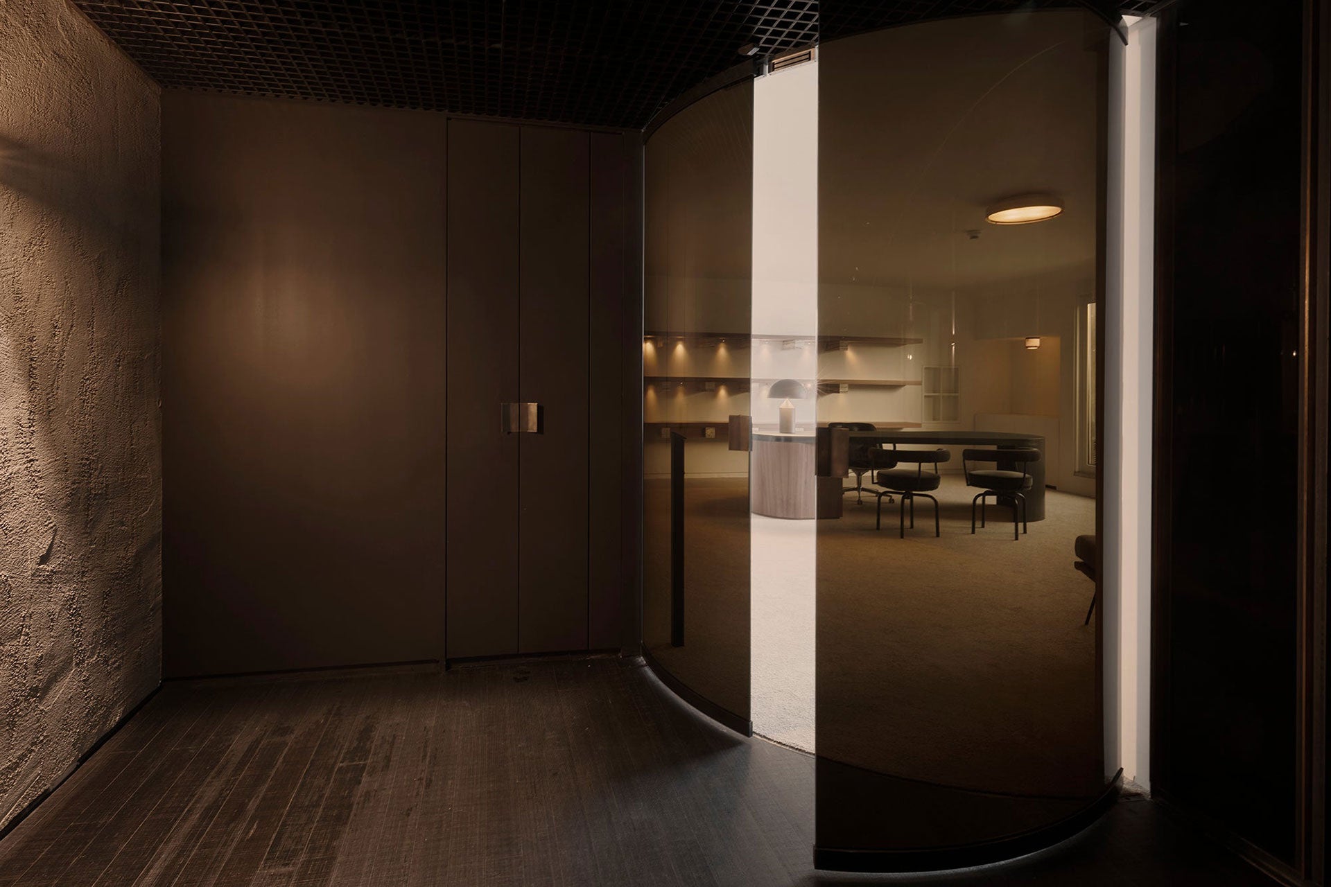 Interior with elegant dark curved glass doors, revealing a bespoke crafted office space beyond.