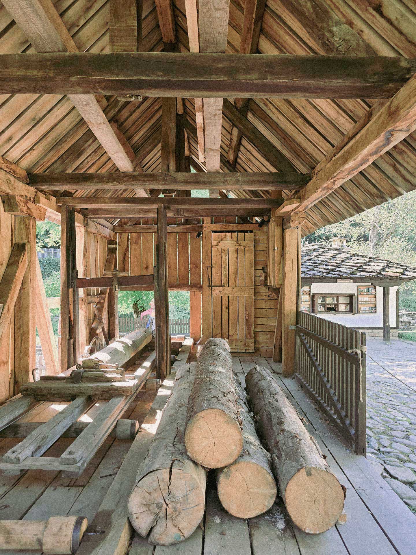 Interior of a traditional wooden house in Bulgaria's Troyan region, featuring giant wooden logs, wooden pallets, and a workshop space for woodcraft.