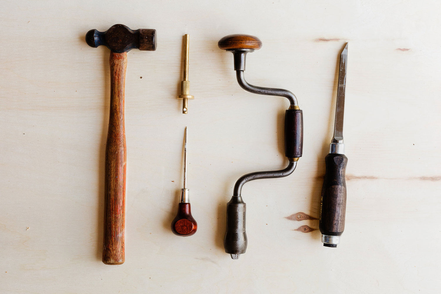 Woodworking tools laid out on a wooden surface, including chisels, drill, and a mallet, arranged neatly for use.